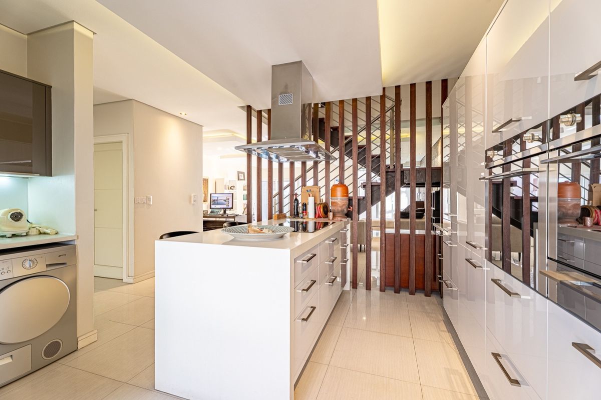Modern kitchen featuring a central island with integrated hob, high-gloss cabinetry, built-in appliances, and a stylish timber slat divider adjacent to the staircase.