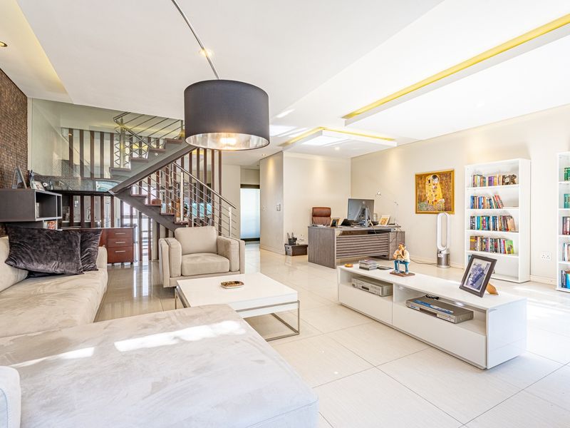 Spacious open-plan living area featuring modern tiled flooring, a striking feature wall, and a contemporary staircase with a glass balustrade.