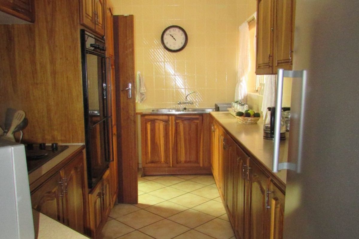 A functional galley-style kitchen featuring traditional wooden cabinetry, tiled backsplash, and built-in oven, offering a classic layout with ample storage space.