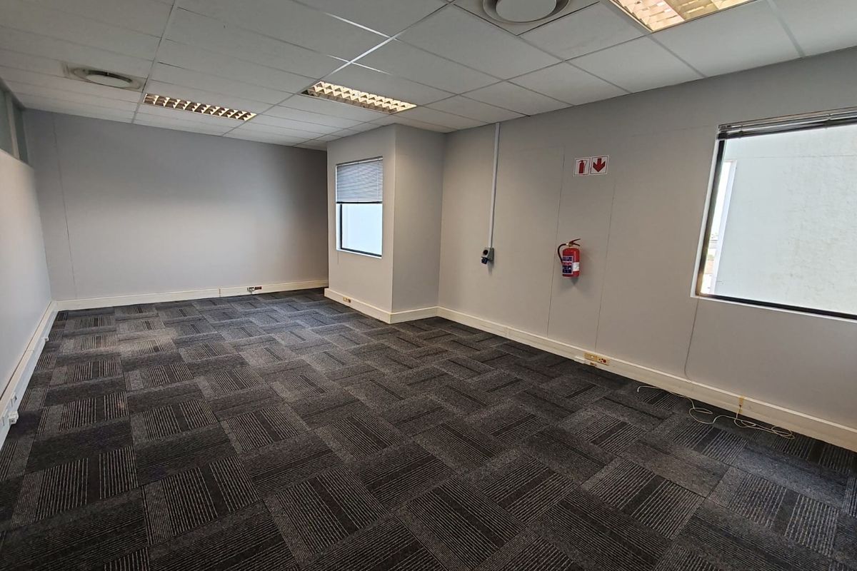 A clean, vacant office space featuring carpet tiles, suspended ceilings with recessed lighting, and functional wall-mounted electrical and fire safety infrastructure.