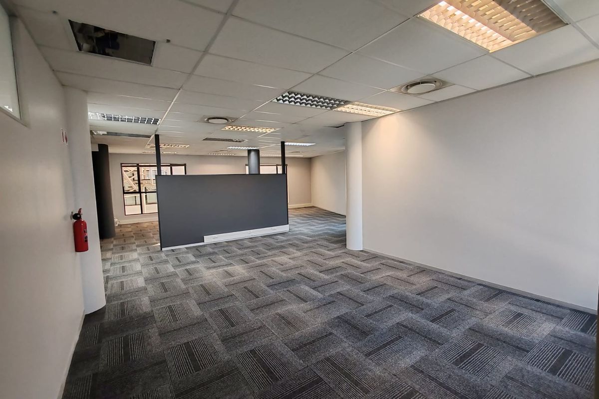 An open-plan office space featuring carpet tiles, a suspended ceiling with recessed lighting, and a central partition wall.