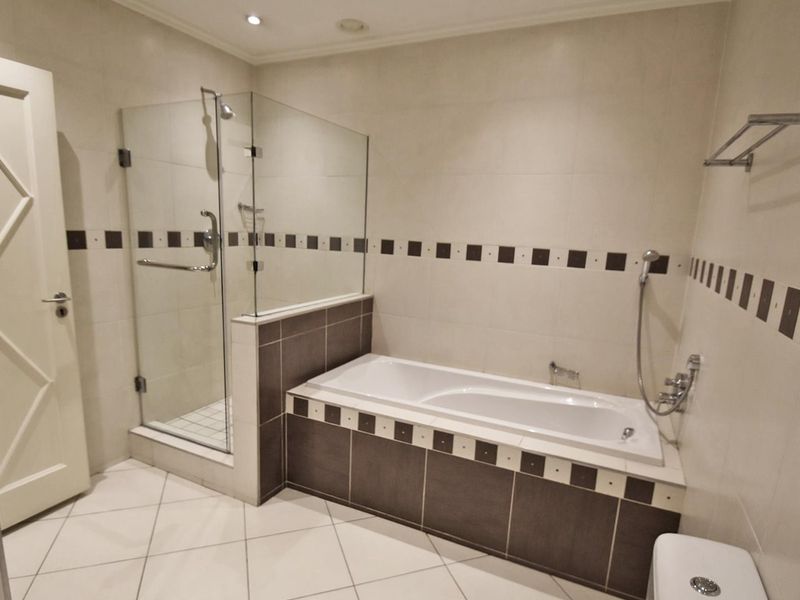 A clean, well-maintained bathroom featuring a built-in bathtub, a separate glass-enclosed shower, and neutral tiled finishes throughout.