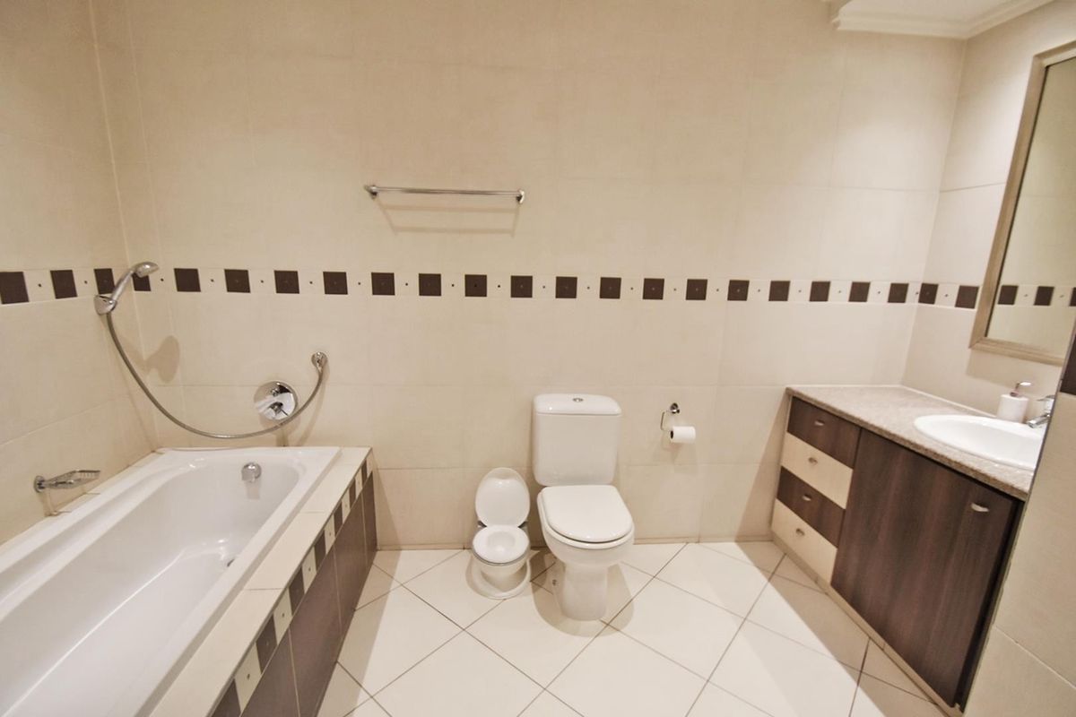 A clean, neutral-toned bathroom featuring a built-in bathtub, a vanity with integrated sink, and tiled finishes throughout.