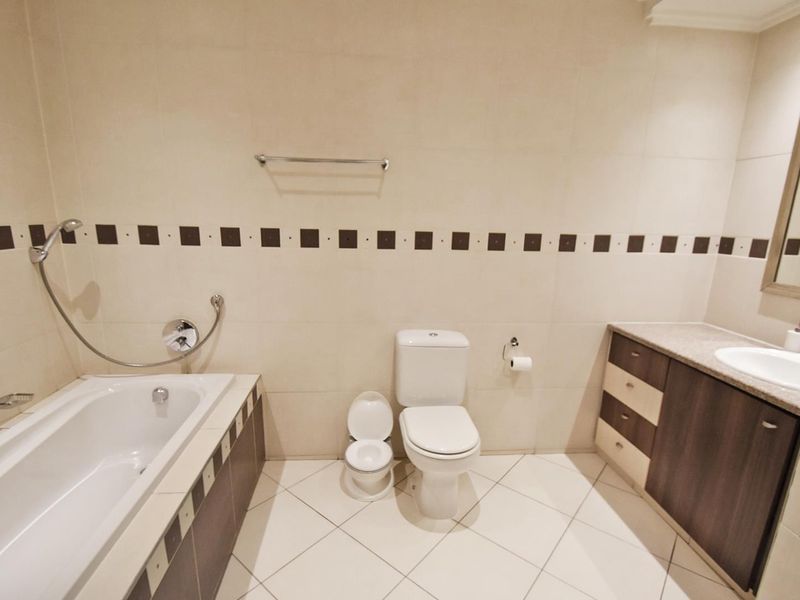 A clean, neutral-toned bathroom featuring a built-in bathtub, a vanity with integrated sink, and tiled finishes throughout.