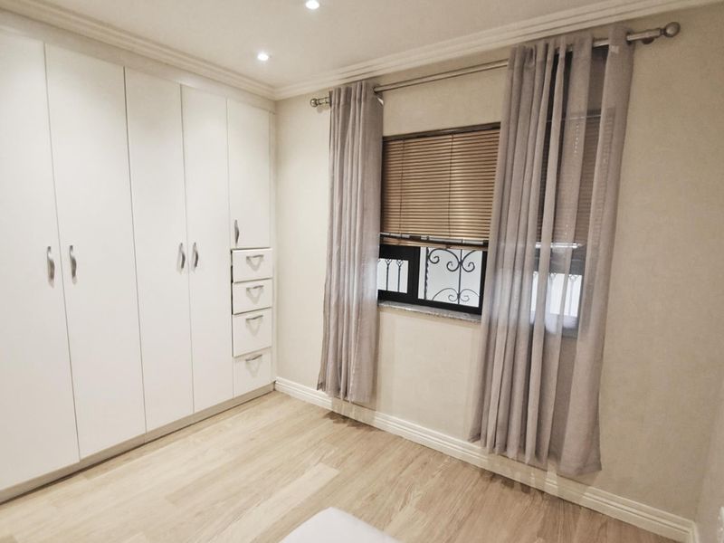 A clean, well-maintained bedroom featuring light laminate flooring, ample built-in cupboard storage, and recessed ceiling lighting.
