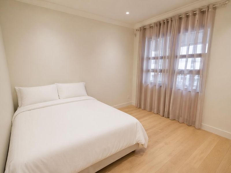 A bright and neutral bedroom featuring light-toned laminate flooring, recessed downlighting, and elegant cove cornicing, creating a clean and inviting living space.