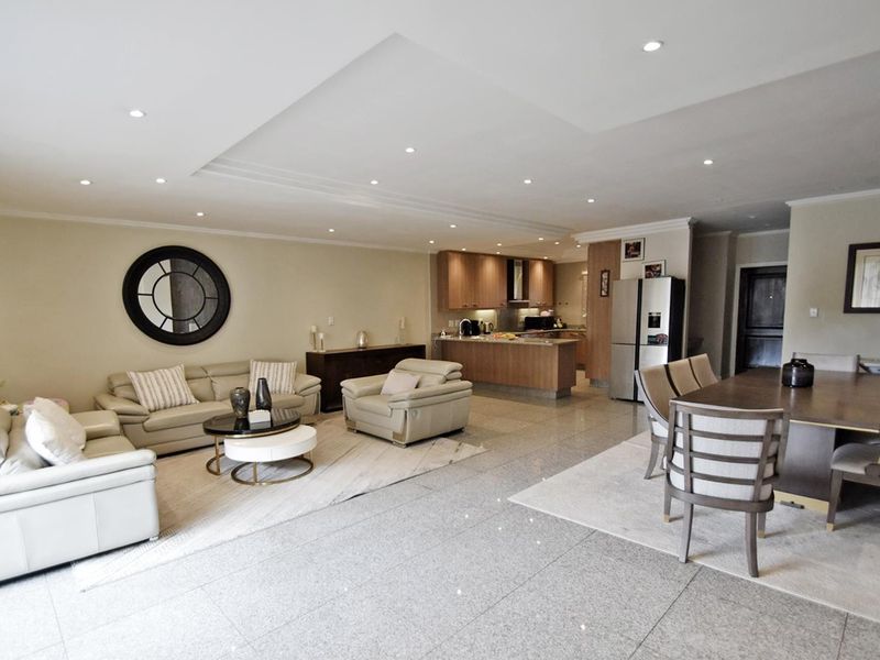 Spacious open-plan living and dining area featuring polished stone flooring, recessed ceiling lighting, and a modern kitchen with integrated cabinetry.