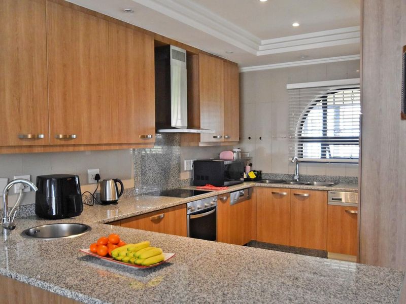 A functional kitchen featuring wood veneer cabinetry, granite countertops, built-in oven, electric hob, and a double sink with an arched window.