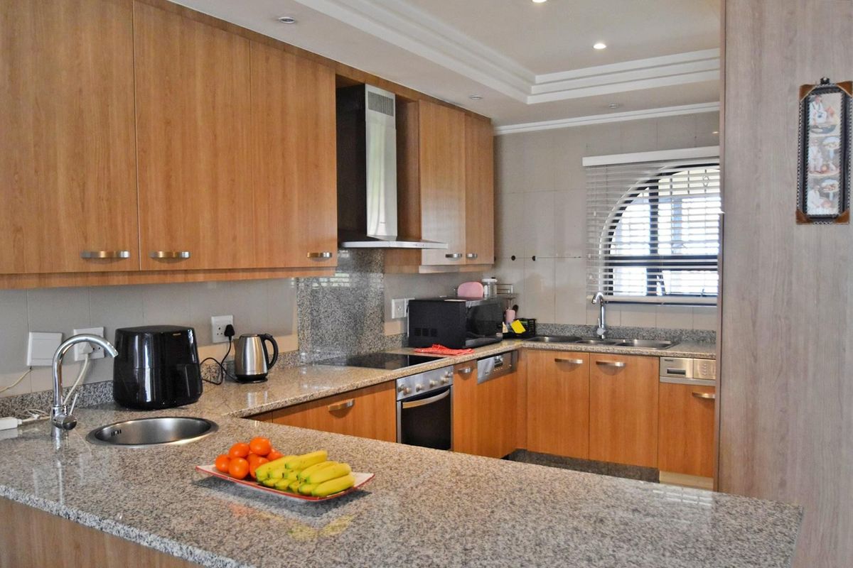 A functional kitchen featuring wood veneer cabinetry, granite countertops, built-in oven, electric hob, and a double sink with an arched window.
