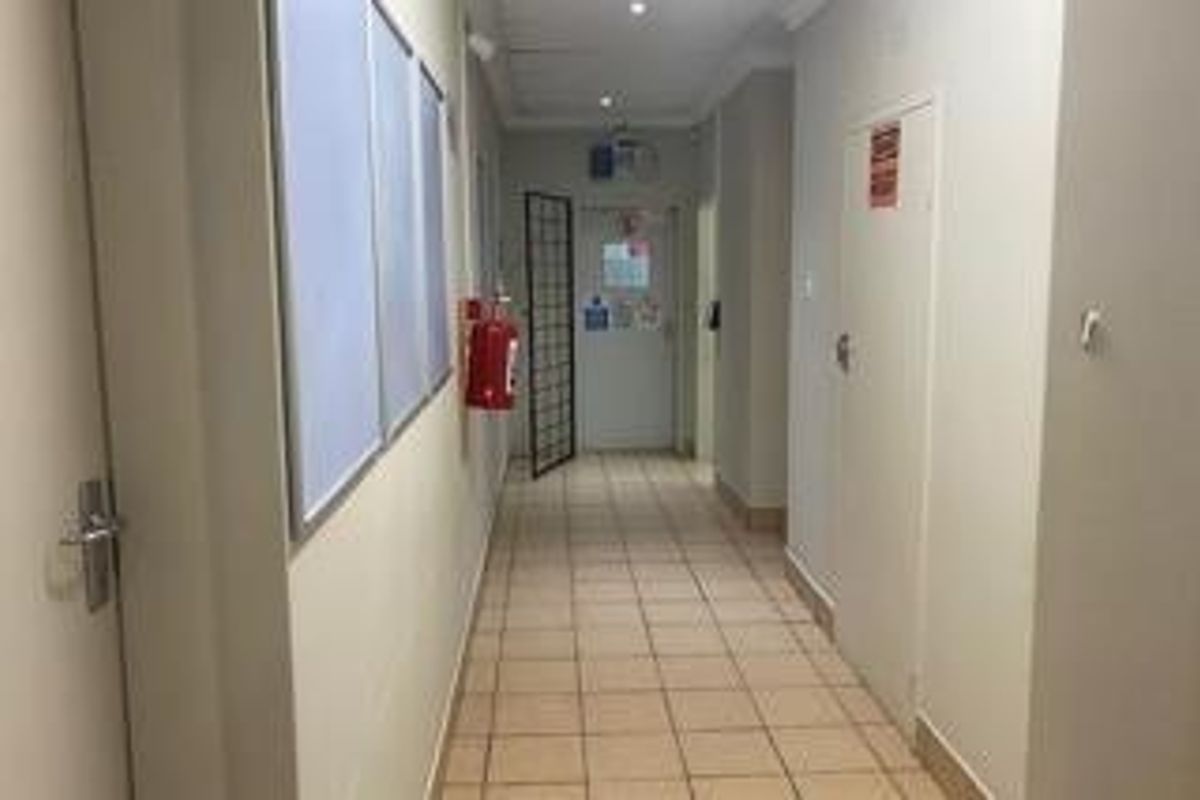 A functional commercial hallway featuring tiled flooring, recessed lighting, and a wall-mounted fire extinguisher, leading to a secure access door.