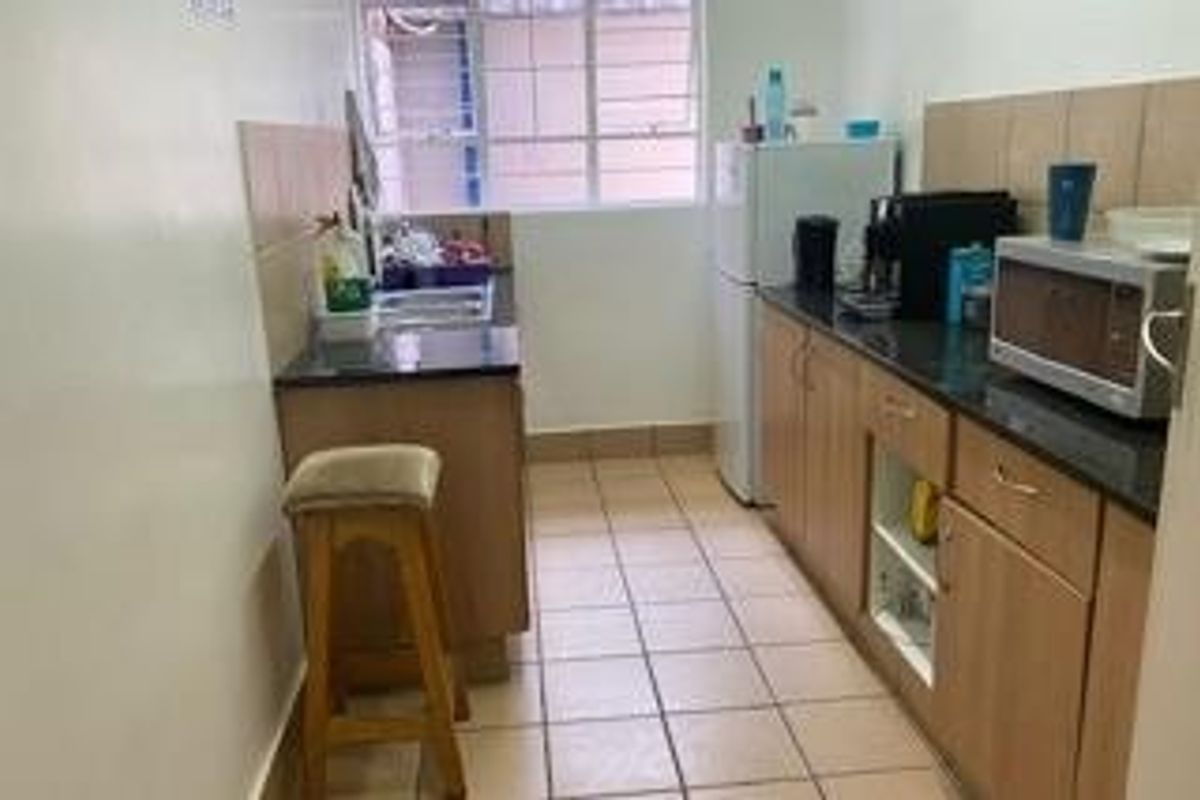 A compact galley-style kitchen featuring built-in wooden cabinetry, granite countertops, and tiled flooring, providing a functional workspace with natural light.
