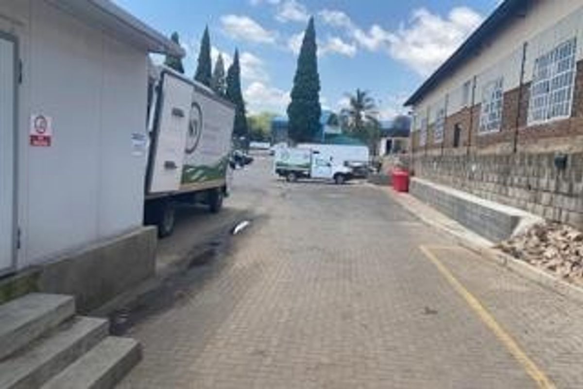 Rear exterior service area featuring paved driveway, retaining wall, and security fencing, suitable for commercial loading and access.
