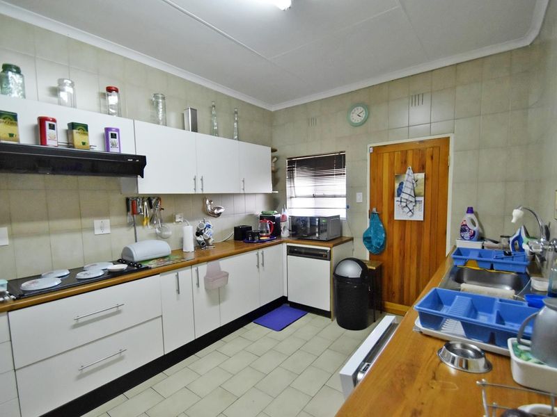 Functional kitchen featuring white cabinetry, laminate countertops, a built-in hob with extractor fan, and tiled splashbacks, offering a practical layout for daily use.