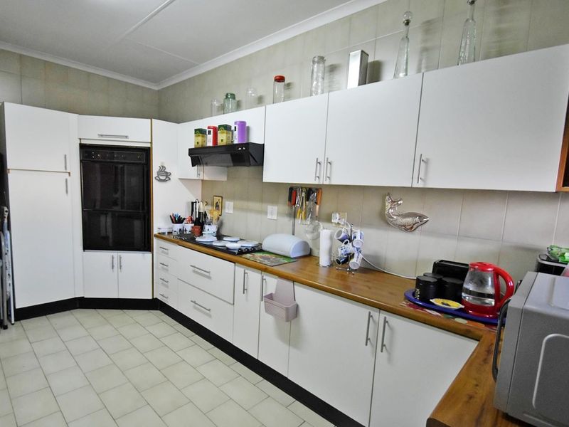 A functional kitchen featuring white cabinetry, wood-look laminate countertops, a built-in oven, and tiled backsplash with neutral floor tiles.