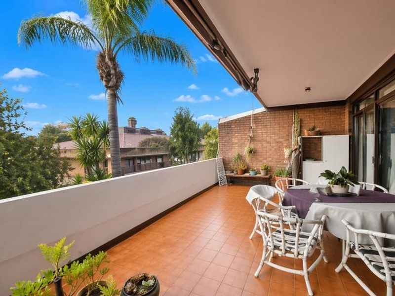 Spacious covered balcony featuring brick walls, tiled flooring, and a retractable awning, offering an ideal outdoor space for relaxation and entertaining.