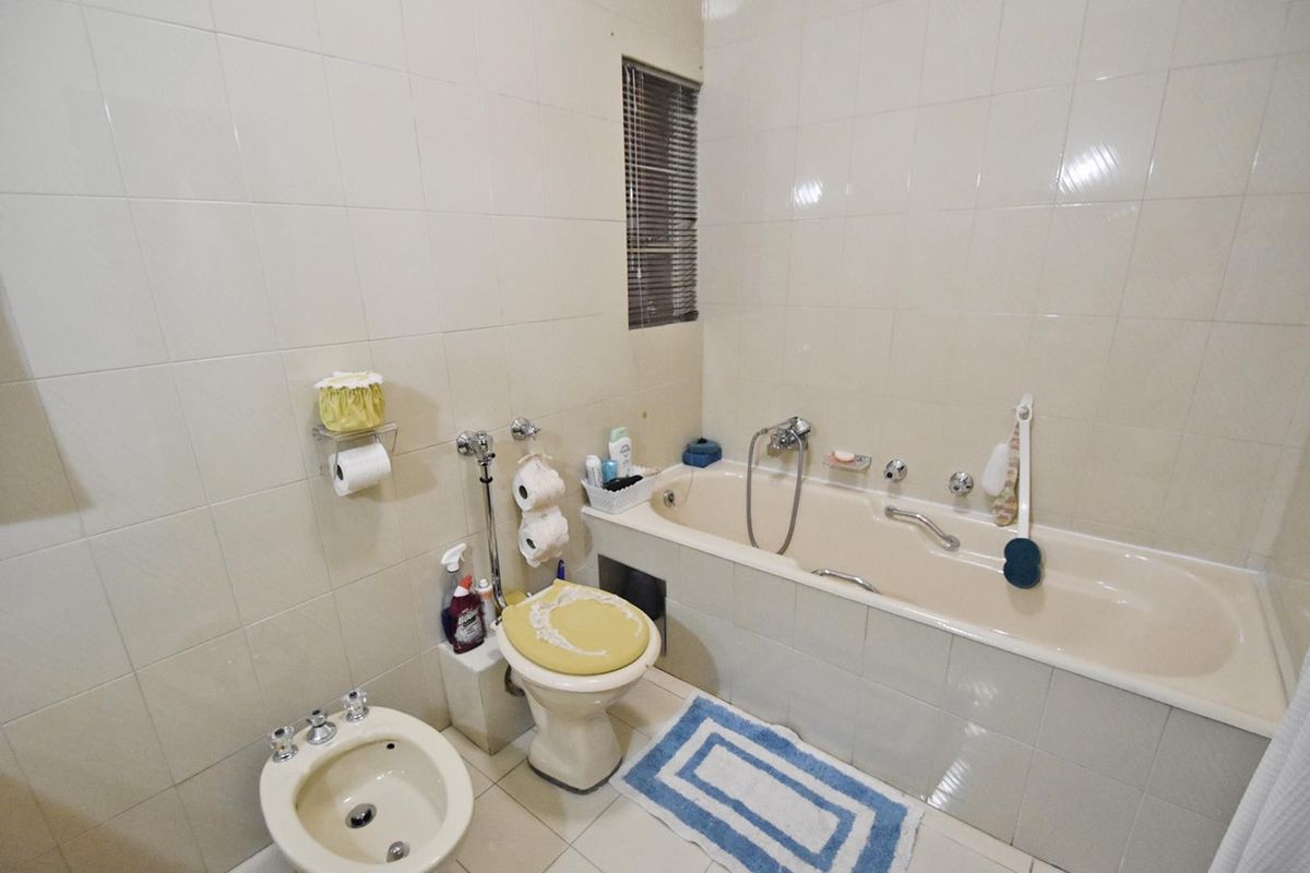A functional bathroom featuring a bathtub, bidet, and toilet with full-height wall tiling and a small window.