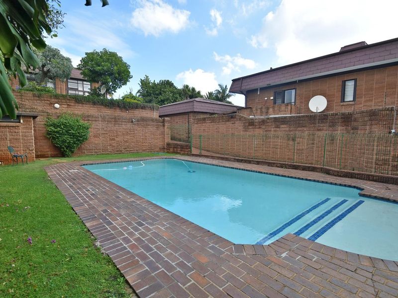 Outdoor swimming pool area featuring brick paving, a surrounding lawn, and high brick boundary walls for privacy.