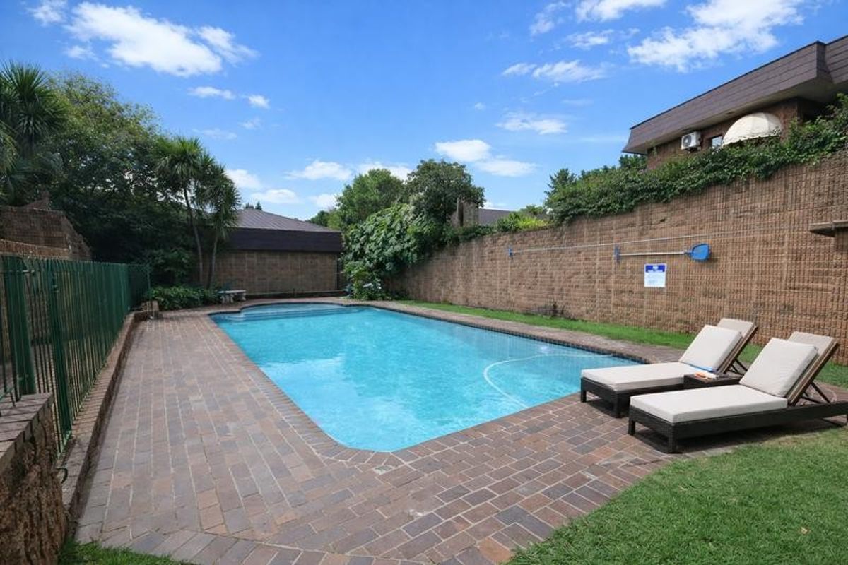 A well-maintained outdoor swimming pool area featuring brick paving, secure metal fencing, and high boundary walls for privacy.