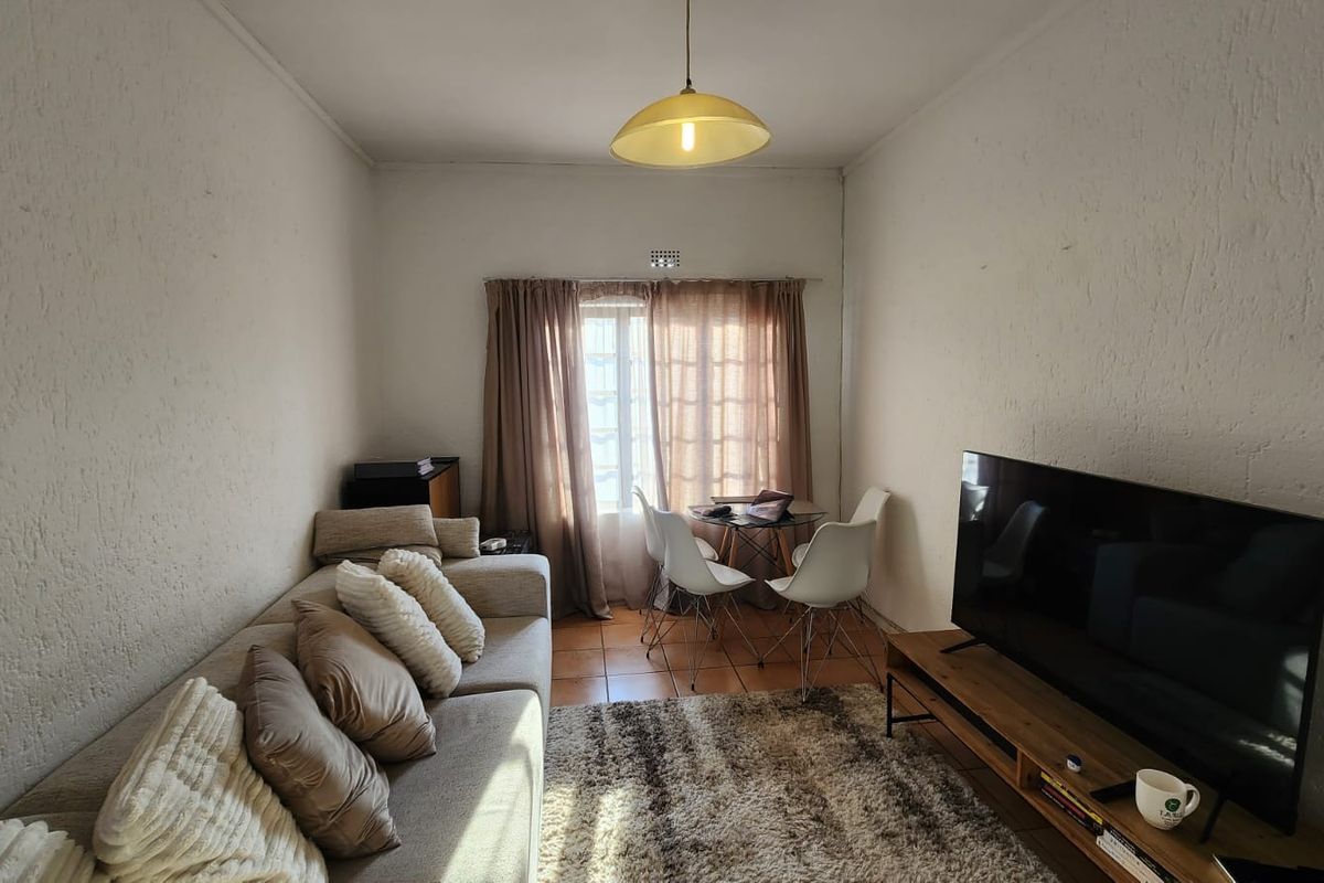 A living room featuring textured walls, terracotta floor tiles, and a central pendant light, offering a functional and comfortable living space.