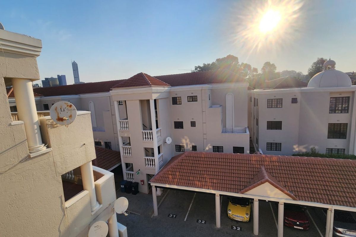 An elevated view of the apartment complex exterior, featuring tiled roofing, covered parking bays, and residential balconies.