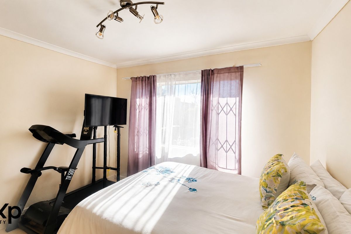 A well-lit bedroom featuring neutral walls, ceiling-mounted track lighting, and a window fitted with a security gate.