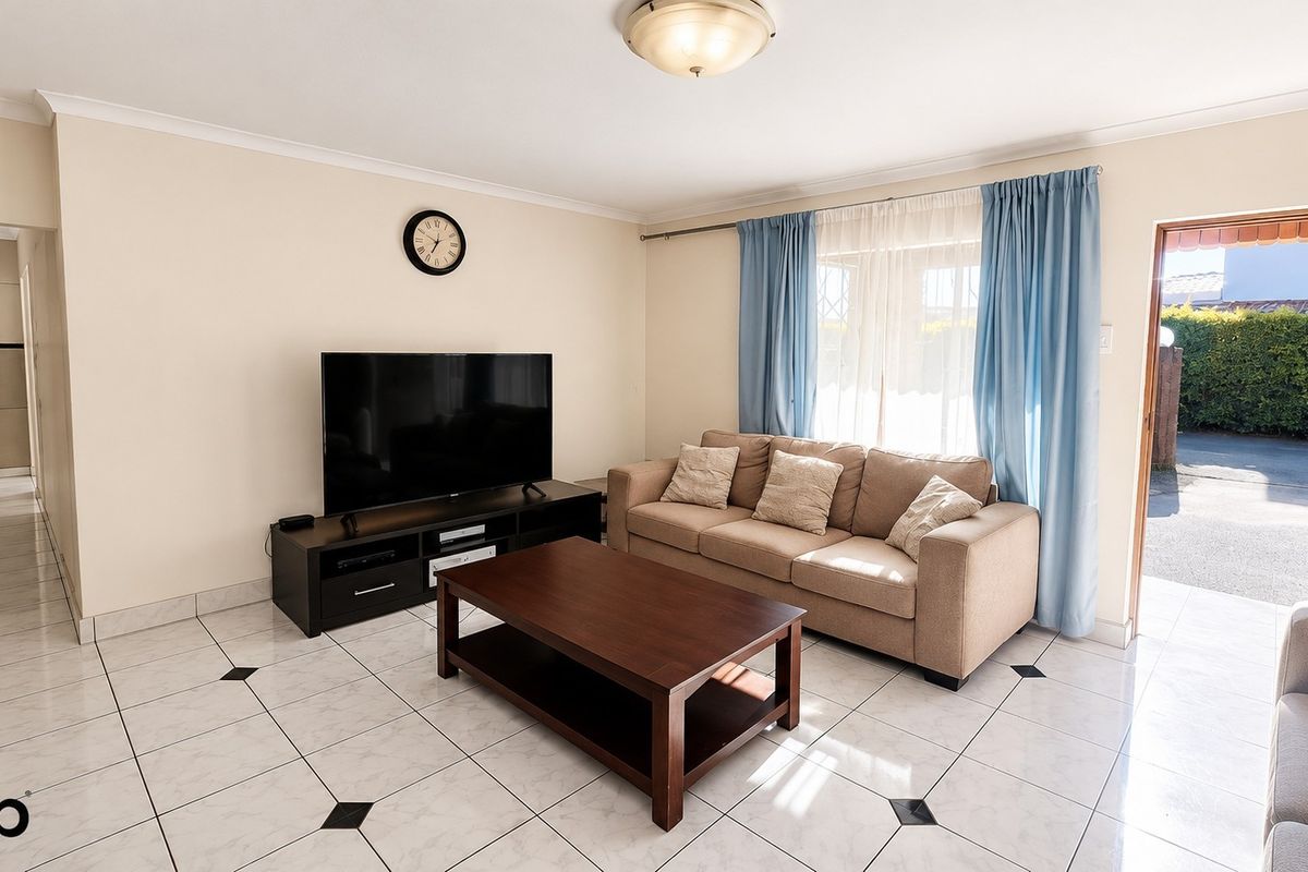 A bright living room featuring tiled flooring, cove cornicing, and direct access to the exterior through a security gate.