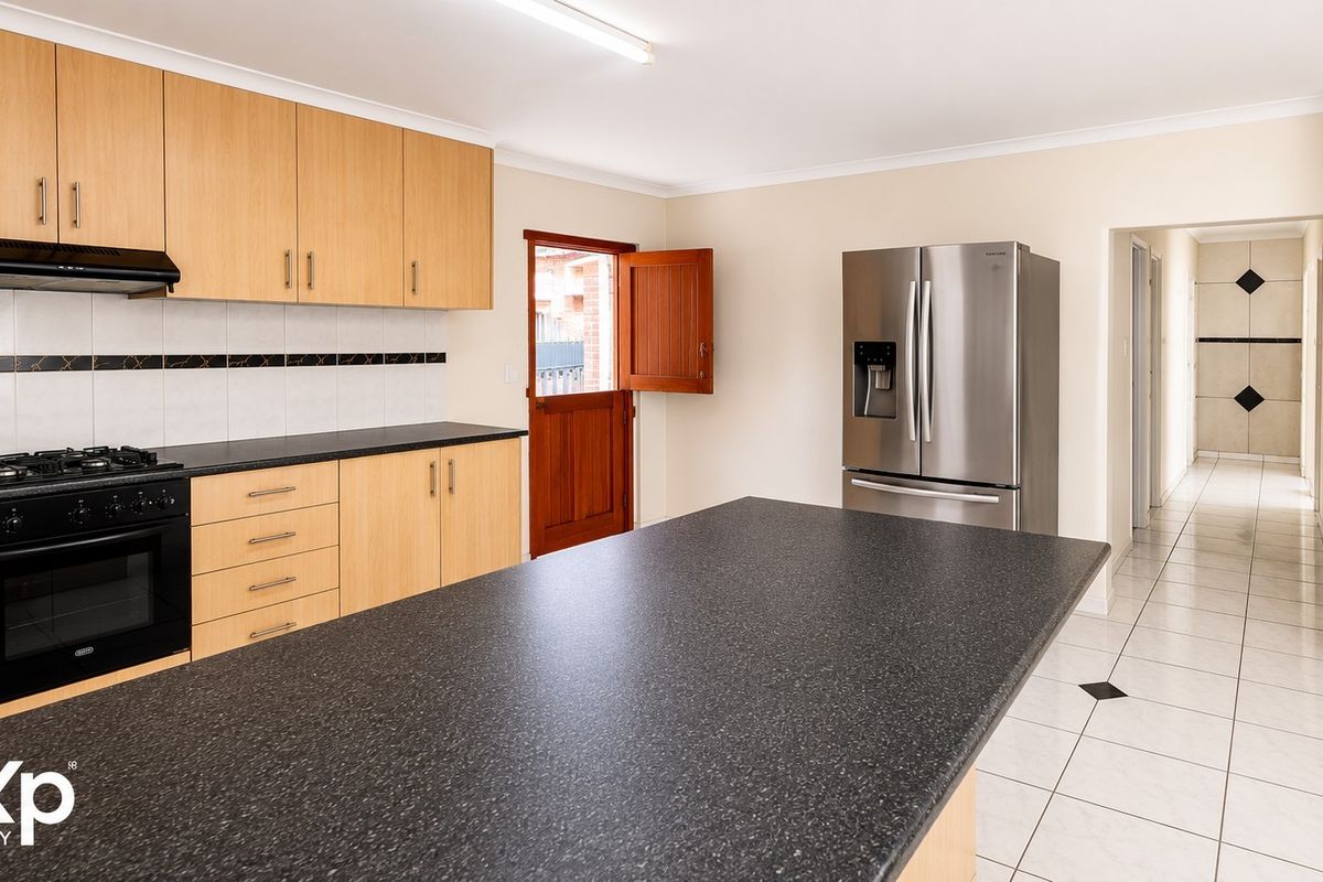 A functional kitchen featuring light wood cabinetry, dark countertops, a gas hob, and tiled flooring with direct access to the exterior.