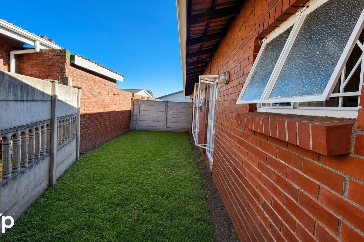A private rear garden area featuring a brick exterior wall, lawn, and precast concrete boundary fencing.