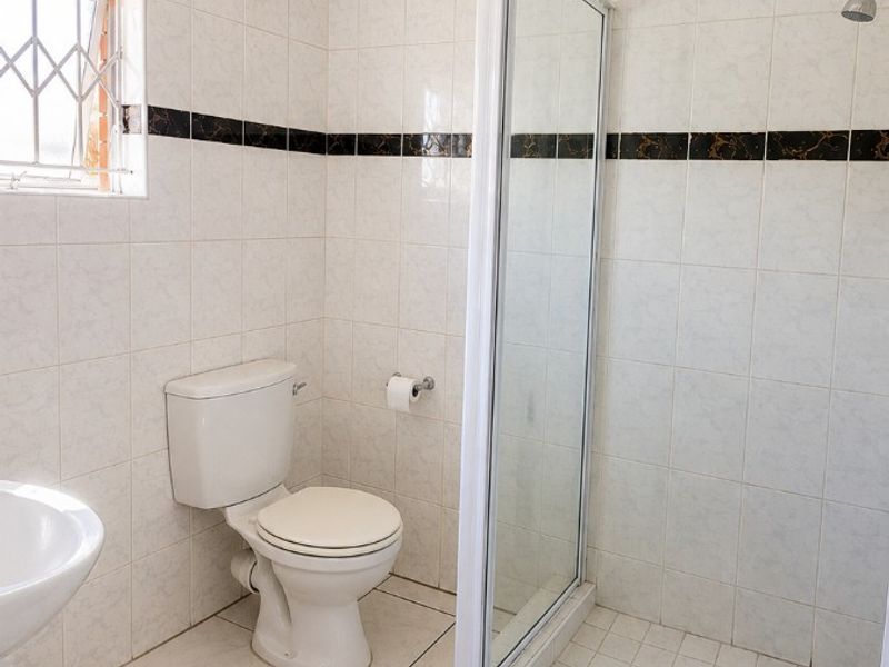 A functional bathroom featuring a shower enclosure, toilet, and pedestal basin with neutral wall and floor tiling.
