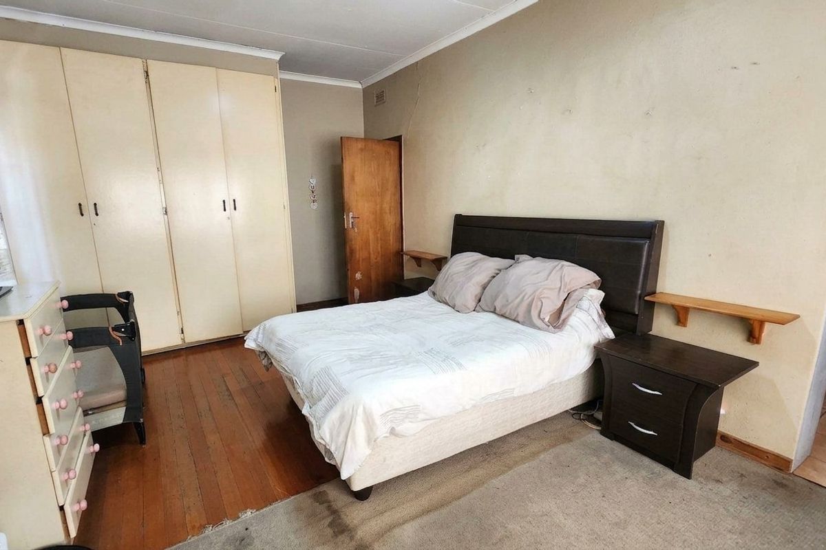 A bedroom featuring timber flooring, built-in cupboards, and coved ceilings, requiring cosmetic updates to the wall finishes and general maintenance.