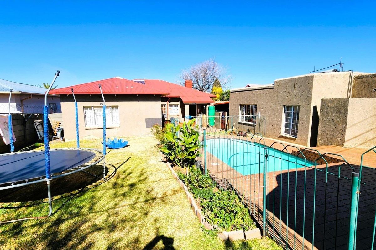 Rear garden area featuring a swimming pool with paved surround, lawn, and perimeter fencing, set against the rear elevation of the house.