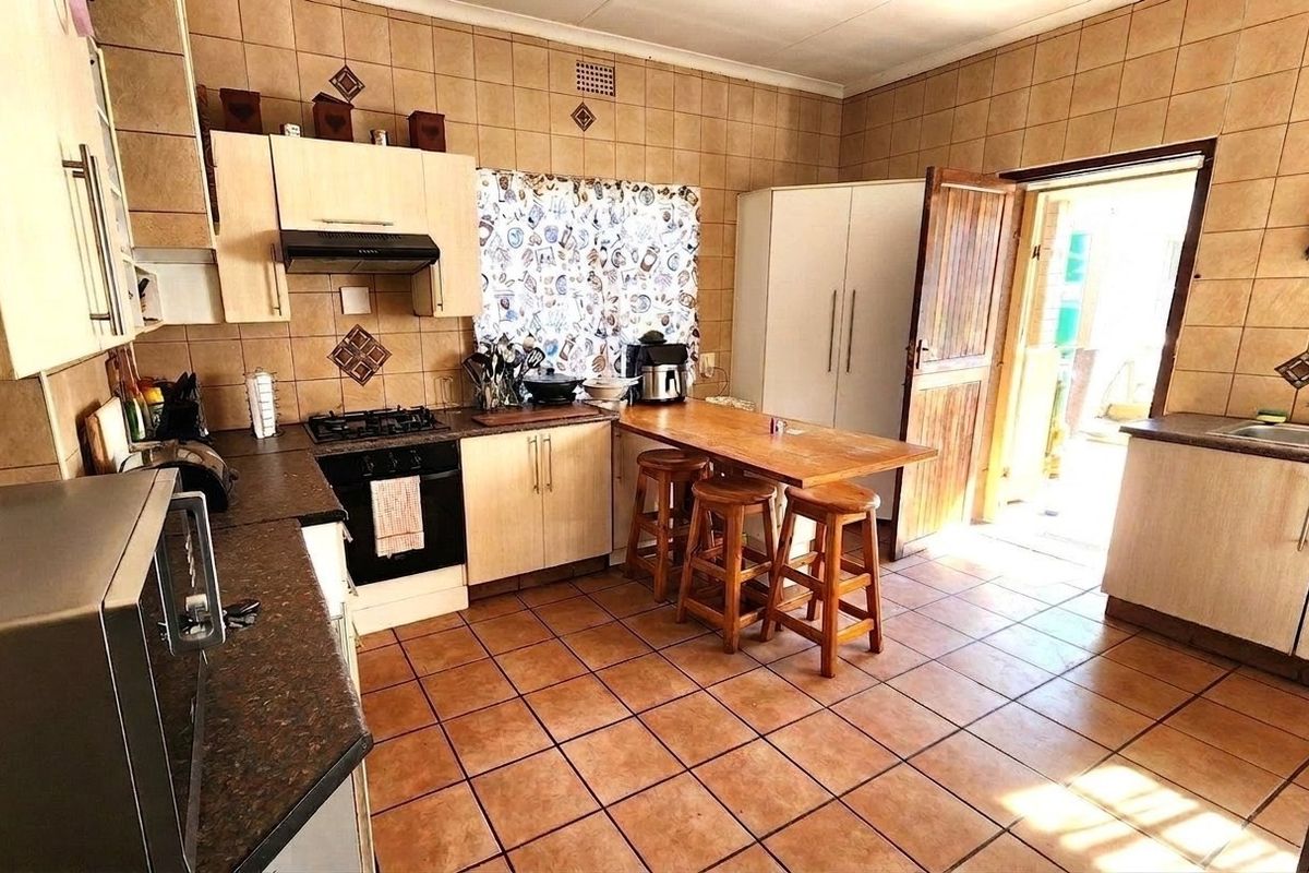 A functional kitchen featuring tiled walls and flooring, built-in cabinetry, a gas hob with extractor fan, and direct access to the exterior.