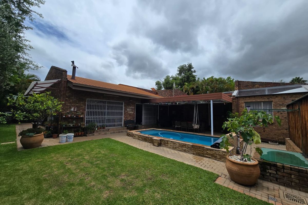 Rear exterior view featuring a brick-faced house, a raised swimming pool, a covered patio area, and a well-maintained lawn.