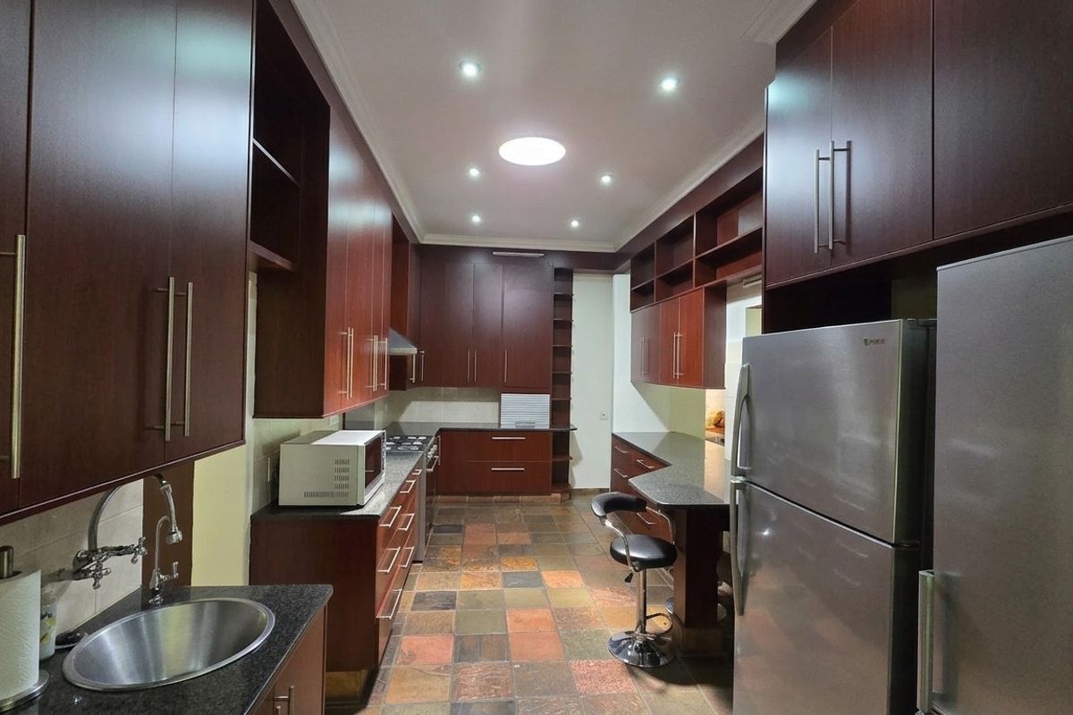 Spacious kitchen featuring dark wood cabinetry, granite countertops, stone tile flooring, and a skylight, providing a functional and well-lit culinary workspace.