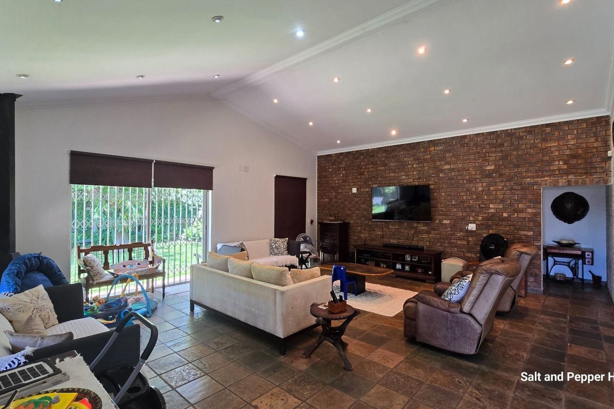 Spacious living room featuring a vaulted ceiling, exposed brick feature wall, tiled flooring, and a freestanding fireplace with access to the garden.