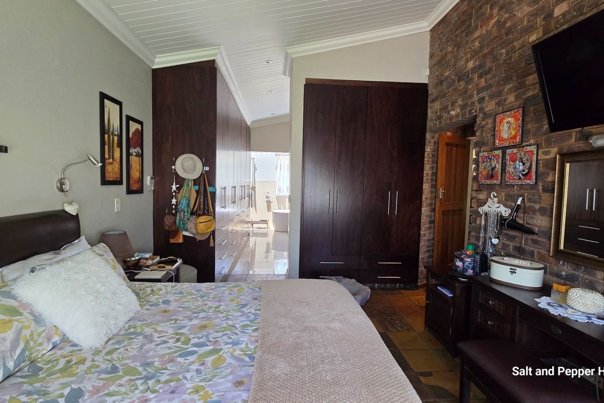 Spacious bedroom featuring extensive built-in cabinetry, an exposed brick feature wall, and a vaulted tongue and groove ceiling with direct access to an en-suite area.