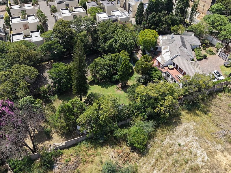 Aerial view of a residential property featuring a large garden with mature trees, paved driveway, and established boundary walls in a suburban setting.
