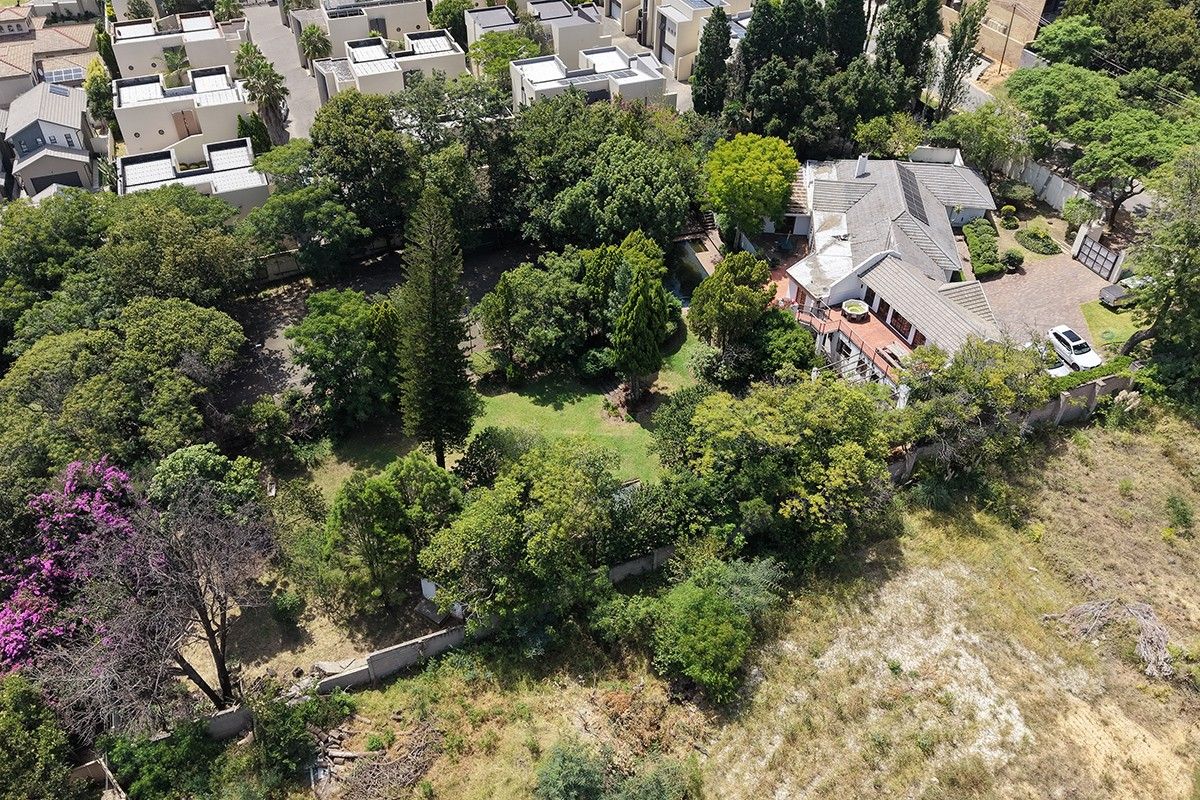 Aerial view of a residential property featuring a large garden with mature trees, paved driveway, and established boundary walls in a suburban setting.