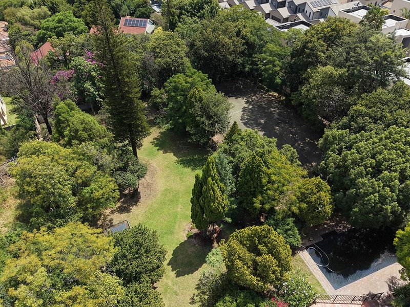 Aerial view of a spacious residential plot featuring established trees, a well-maintained garden, and a swimming pool within a suburban setting.