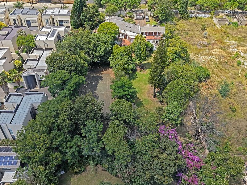 Aerial view of a residential property featuring a private tennis court, extensive mature trees, and established garden space within a secure estate setting.