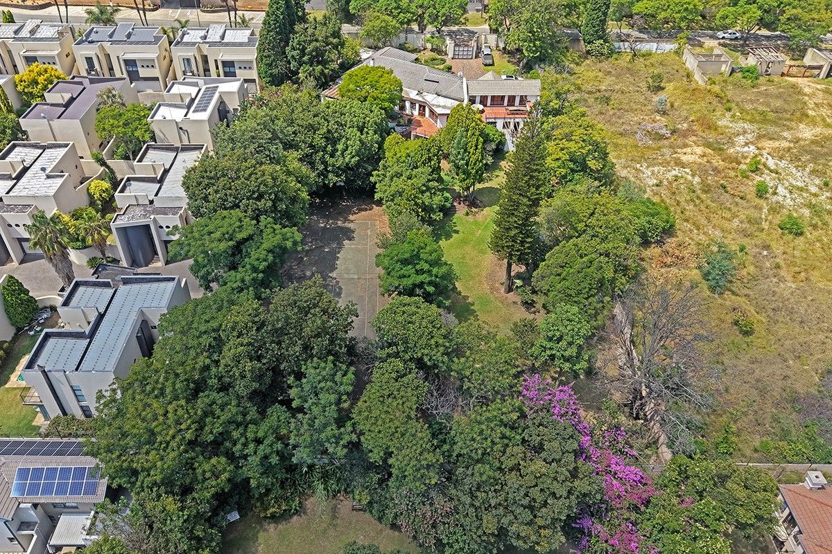 Aerial view of a residential property featuring a private tennis court, extensive mature trees, and established garden space within a secure estate setting.