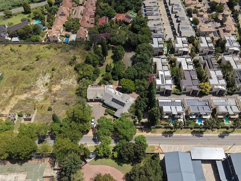 Aerial view of a residential property featuring a main dwelling, established garden, and paved driveway, situated within a suburban neighborhood.