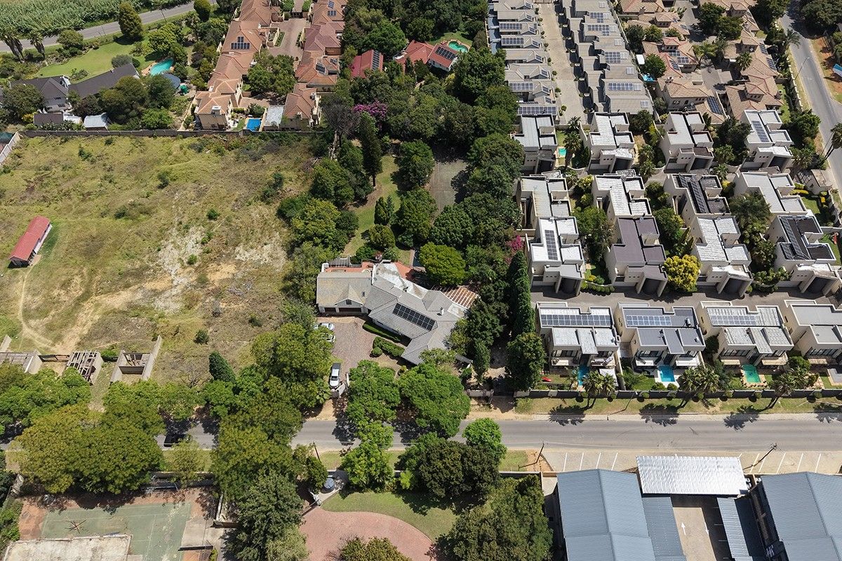 Aerial view of a residential property featuring a main dwelling, established garden, and paved driveway, situated within a suburban neighborhood.