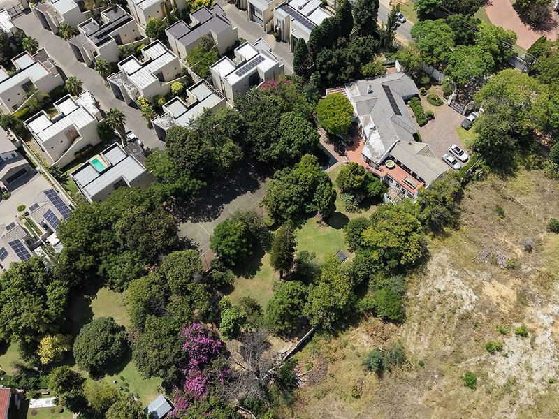 An aerial view of a residential property featuring a large landscaped garden, mature trees, and a paved driveway within a suburban estate setting.