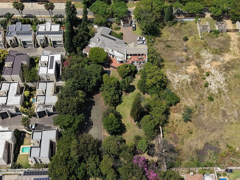 Aerial view of a residential property featuring a large garden, mature trees, and a paved driveway, situated within a suburban neighborhood.