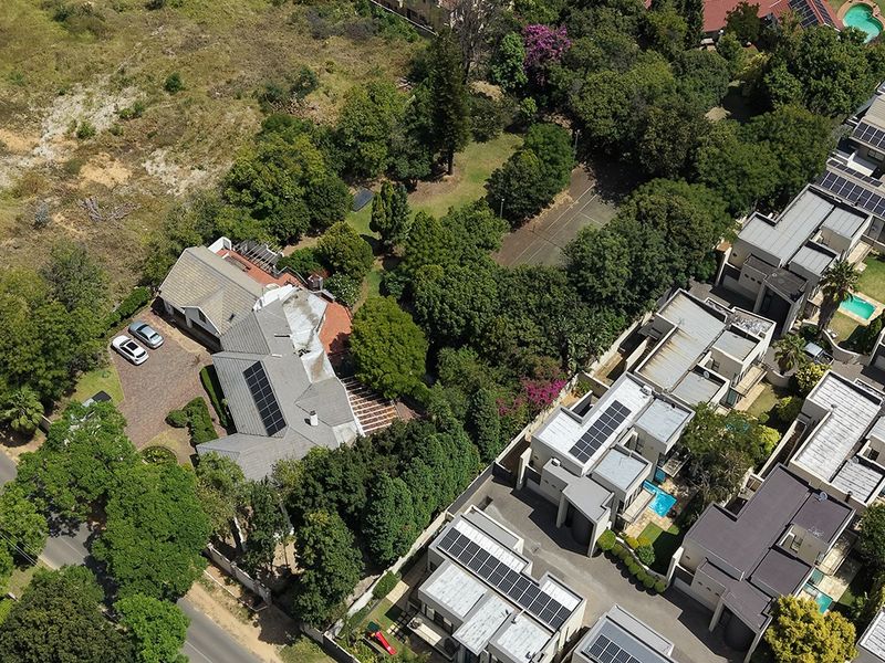 Aerial view of a residential property featuring a tiled roof with solar panels, a paved driveway, and established garden surroundings within a suburban estate.