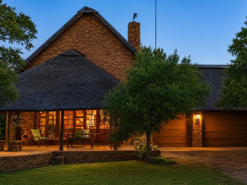 A charming thatched-roof residence featuring a spacious covered patio, brick exterior, and integrated garage, set within a well-maintained garden environment.