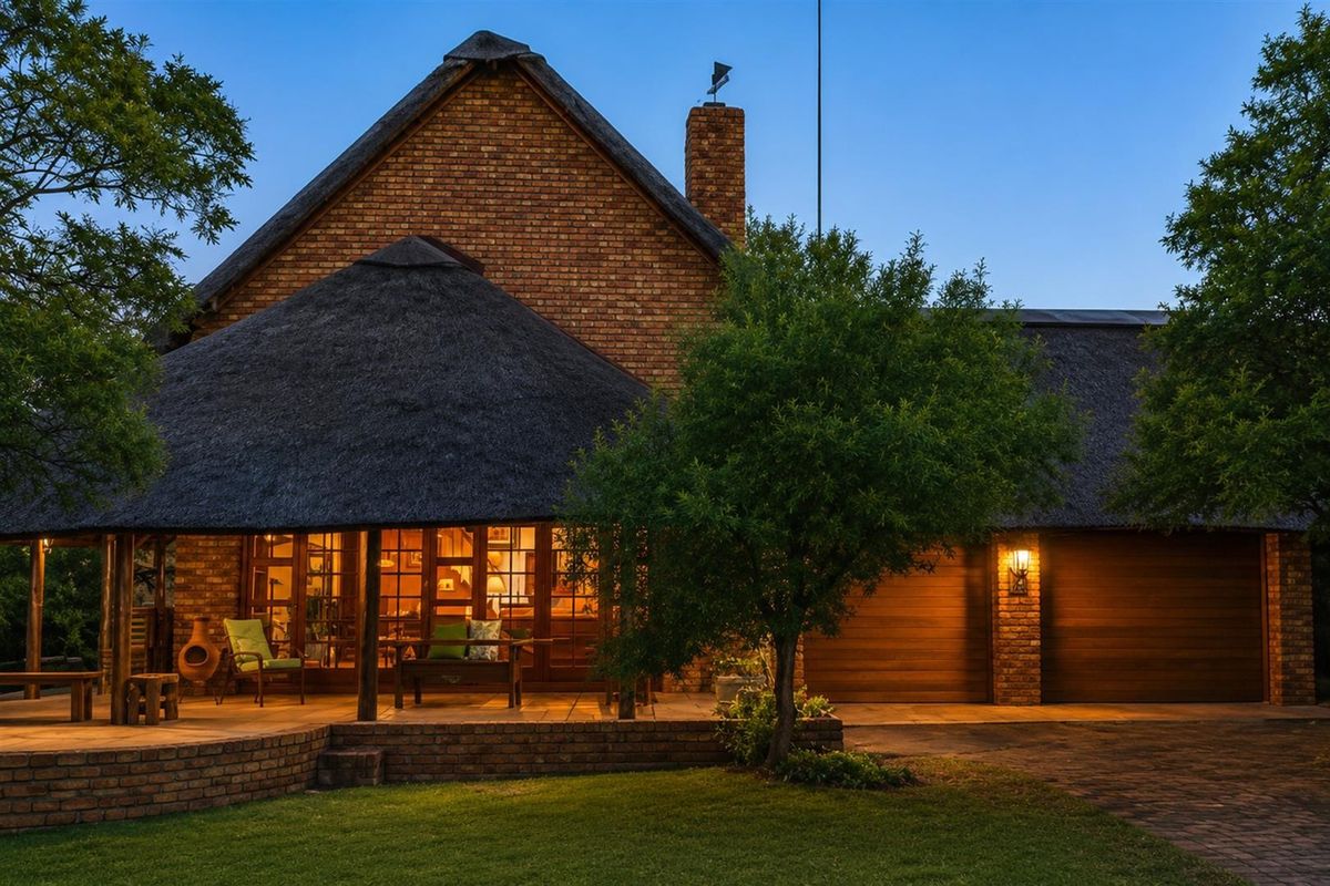A charming thatched-roof residence featuring a spacious covered patio, brick exterior, and integrated garage, set within a well-maintained garden environment.