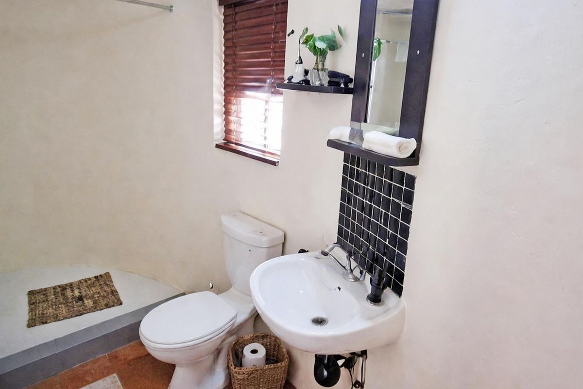 A functional bathroom featuring a pedestal basin with a tiled splashback, a toilet, and a dedicated shower area with natural light from a window.