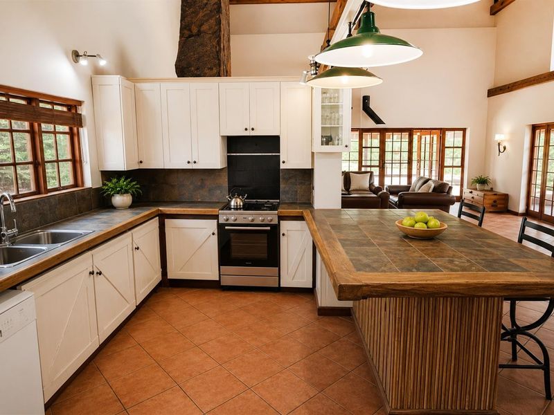 Spacious open-plan kitchen featuring white cabinetry, tiled countertops, a central island, and exposed timber beams, seamlessly flowing into the adjacent living area.